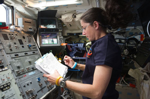 NASA astronaut Nicole Stott, STS-133 mission specialist, reads a procedures checklist on the aft flight deck of space shuttle Discovery while docked with the International Space Station.